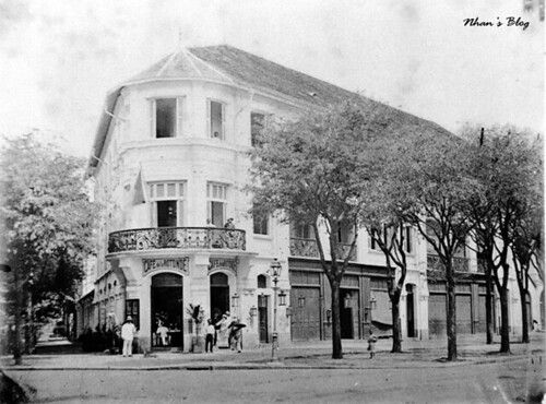 01 Cafe de la Rotonde ở địa chỉ số 2 Catinat. Bên phải bức ảnh là đường Đường Bạch Đằng với hai hàng cây ở một bên hè. Ả