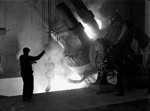 Workman stands beside a furnace at the Stelco Steel Co., directing the pouring of molten steel into a ladle. / Un ouvrie