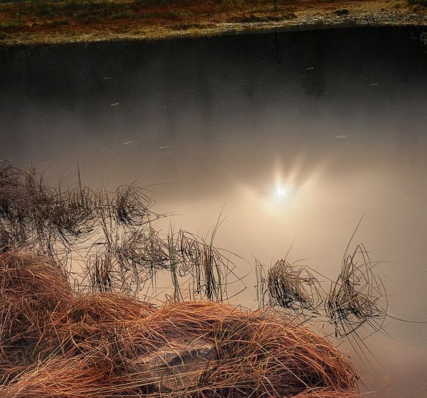 Die Sonne spiegelt sich im dunklen Karsee, Reif liegt über dem Gras.