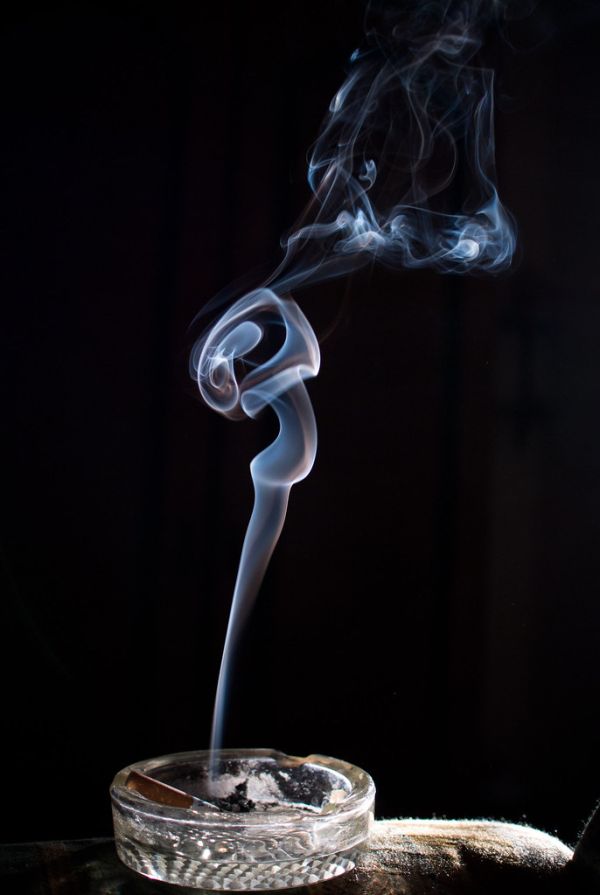 Cigarette in an ash tray with smoke on dark background